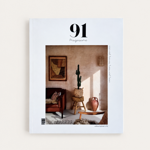 A magazine titled '91 Magazine' shown upright against a light neutral background. The cover features a warm-toned interior scene with a chair, framed artwork, a cactus in a woven planter, and a vase.
