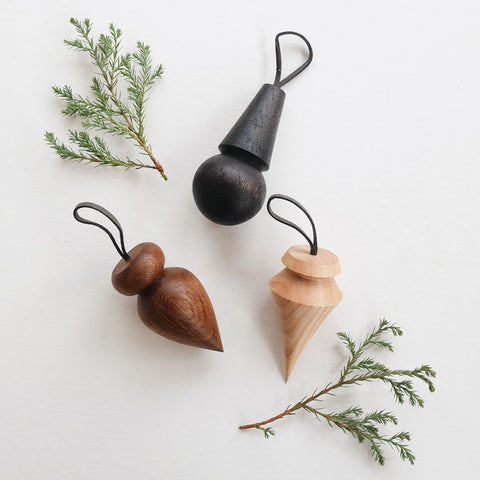 Set of three handmade wooden Christmas baubles in black, brown and natural wood, styled with greenery