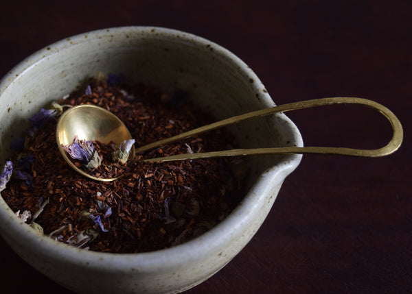 Brass and silver teaspoon with loose leaf tea and ceramic bowl