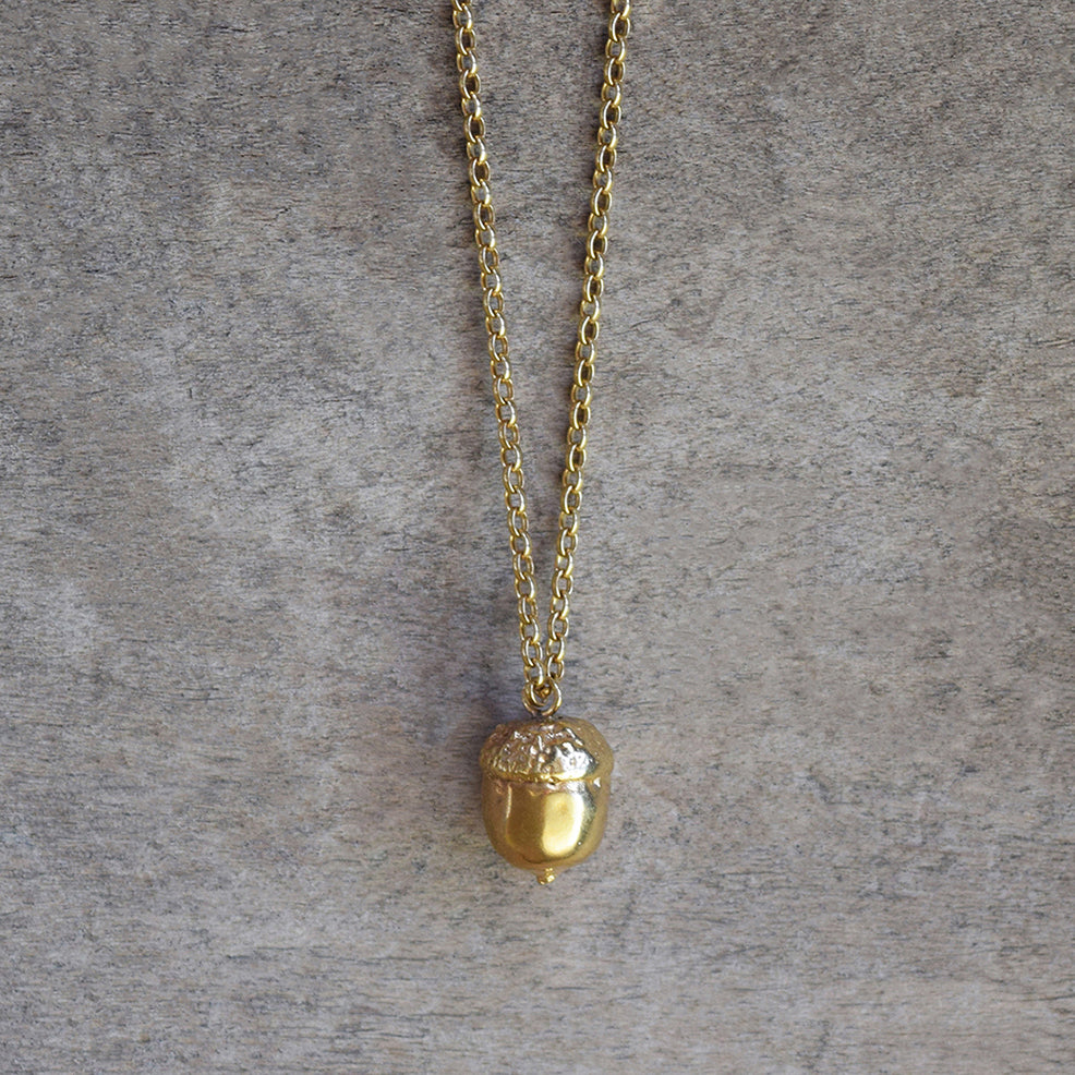 Gold acorn necklace by Alice Stewart Jewellery, handcrafted from sterling silver with 18k gold plating on a natural wood surface