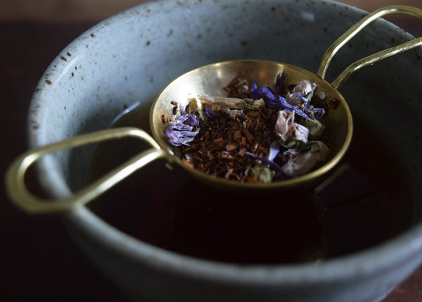 Handmade brass and silver tea strainer by raz|maker with loose feaf tea sitting in a ceramic cup 