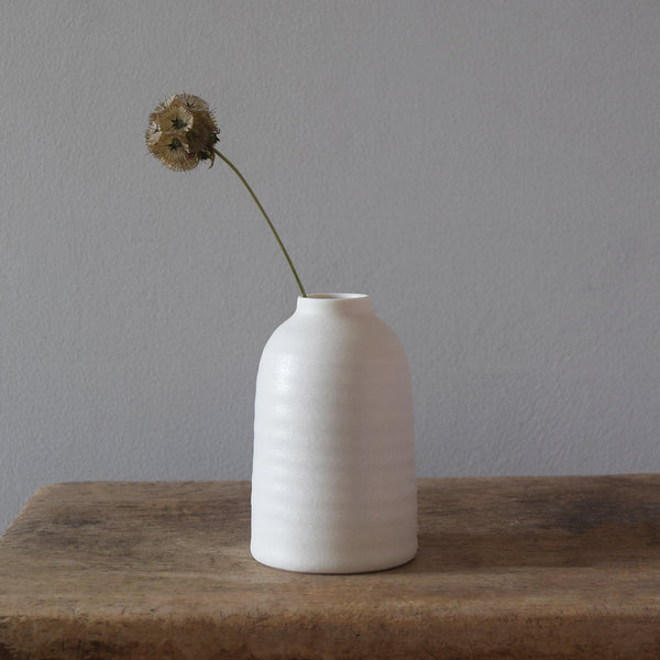Porcelain Bottle Vase wheel thrown by Katie Robbins in her Birmingham studio. Glazed in a matt chalky finish with the makers’ unique leaf stamp on the bottom. Perfect for single stem flowers, small posies and seed heads. 